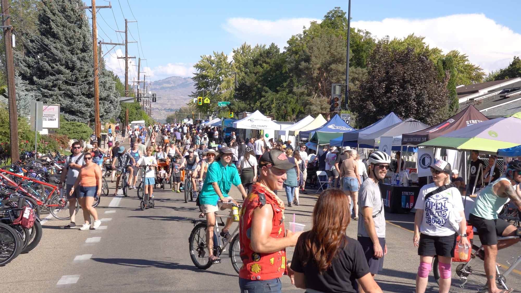 A wide-angle shot of a large crowd of people, families, and cyclists filling Ustick Road in Boise during the Open Streets event.