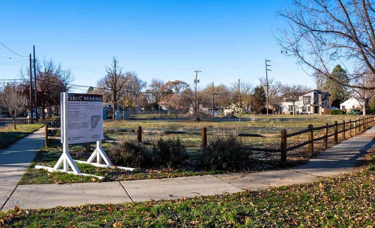 Wide view of a vacant lot in a Boise neighborhood with a public hearing sign in the foreground.