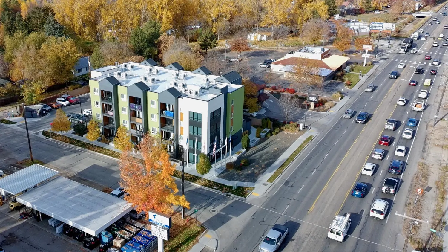 A multi-story apartment building along a busy Boise arterial, shown from above with traffic passing beside it.