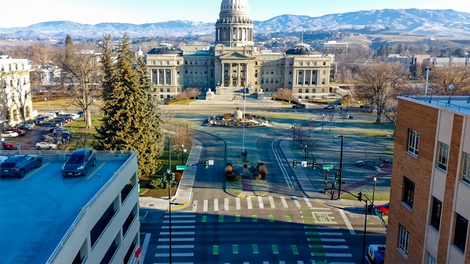 Capitol Square Before Traffic-dominated roadway and intersection in front of the Idaho State Capitol, with wide lanes, crosswalks, and minimal pedestrian gathering space.