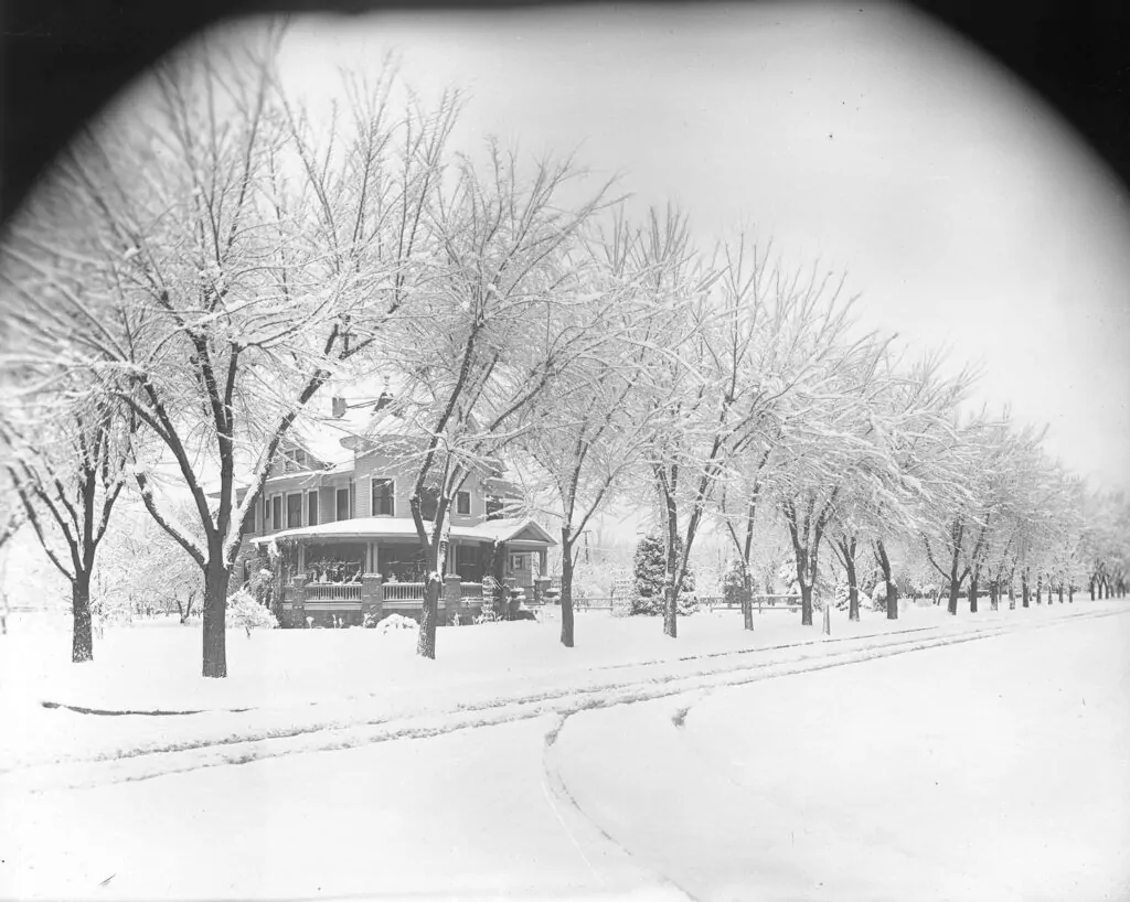 Historic black-and-white photograph of a large early 20th-century home on Harrison Boulevard in Boise, lined with leafless trees and covered in fresh snow, circa 1915–1920.