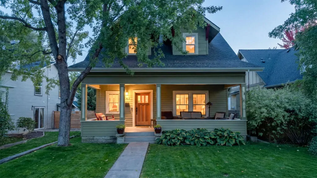 Front porch of a historic North End Boise home at dusk, with warm interior lights visible through windows and a clear path leading from the sidewalk to the entry.