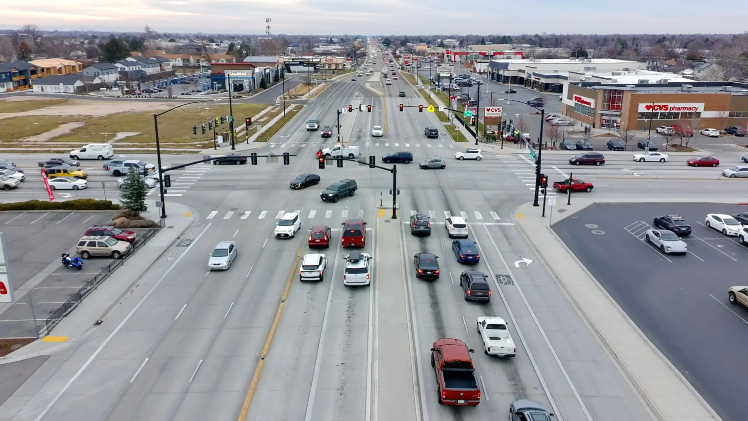 Drone view of a large multi-lane commercial intersection in the Treasure Valley surrounded by parking lots and retail buildings, illustrating suburban sprawl.