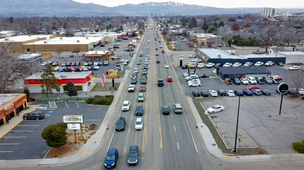 A wide Boise commercial corridor lined with traffic, parking lots, and roadside businesses shows a built environment organized for speed, storage, and throughput.