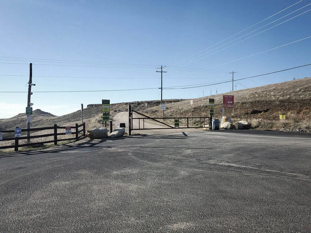 Table Rock access road entrance with a closed gate, overhead utility lines, and multiple warning and no-parking signs near the summit approach.
