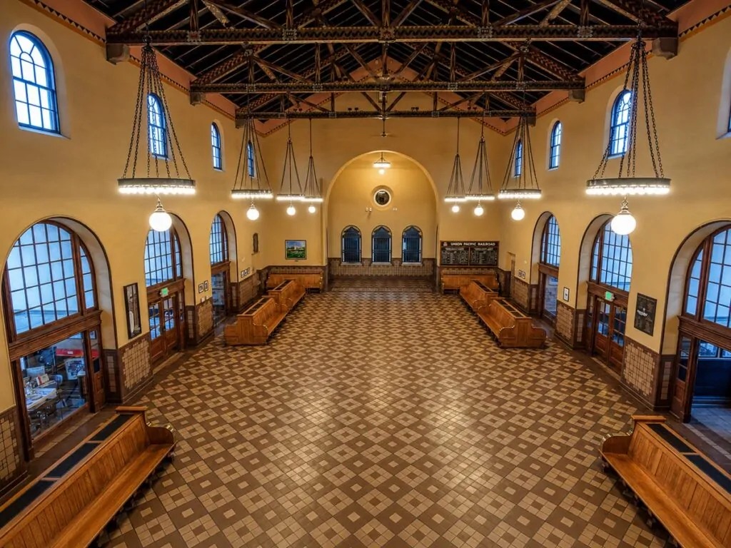 Historic interior of the Boise Depot, with arched windows, wood benches, hanging lights, and a wide tiled hall arranged as a dignified civic room.