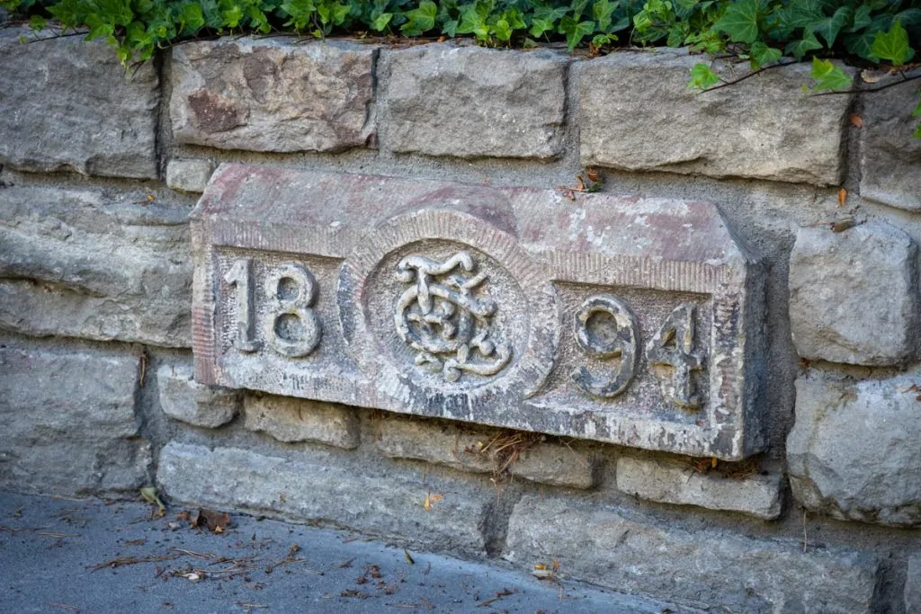 Carved stone block dated 1894 embedded in a stone retaining wall along a sidewalk with ivy in Boise, Idaho.